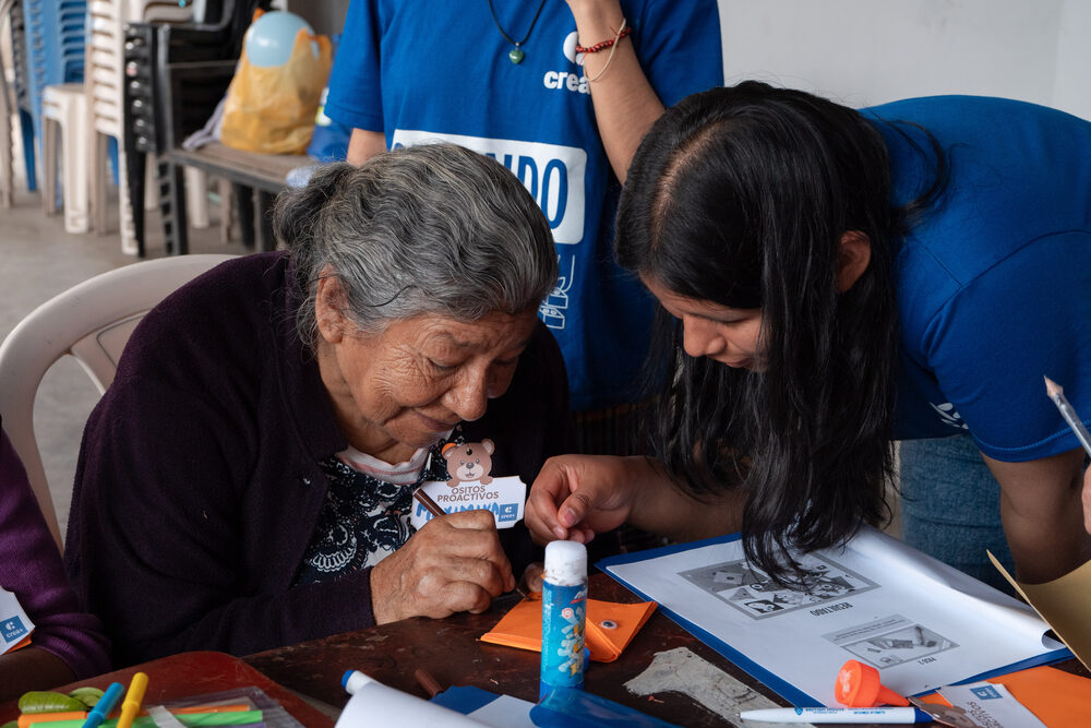 Voluntaria y abuela trabajan juntas en mesa de taller con cabezas pegadas