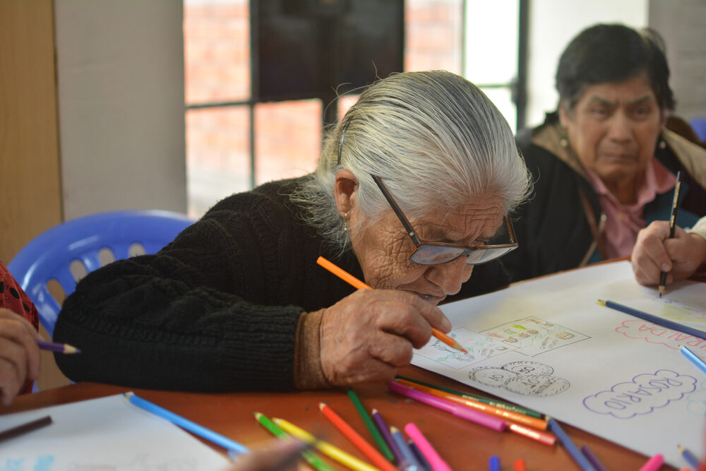Adulta mayor concentrada escribiendo en taller del programa