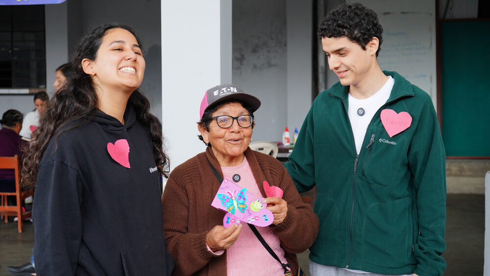 Trio voluntario-adulto-mayor-voluntaria sonríen sosteniendo flores hechas