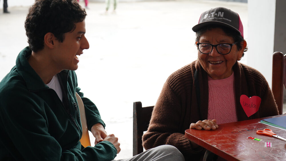 Voluntario joven conversa atentamente con adulta mayor sobre la mesa