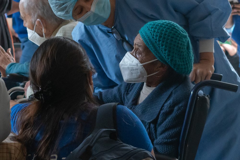 Voluntaria de Crea+ acompaña a adulta mayor en silla de ruedas durante atención sanitaria con personal médico