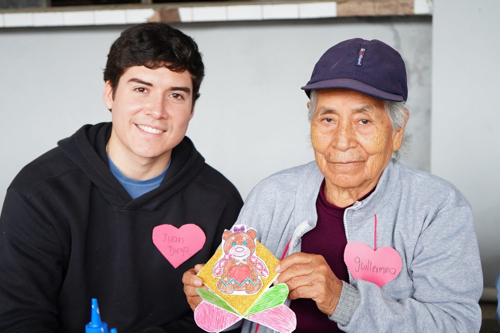 Voluntario joven y adulto mayor varón se miran sonrientes en conexión cálida