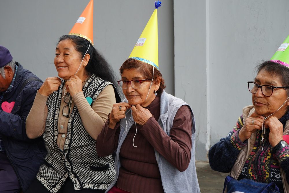 Grupo de adultos mayores celebrando con globos y gorros de fiesta durante el cierre del taller