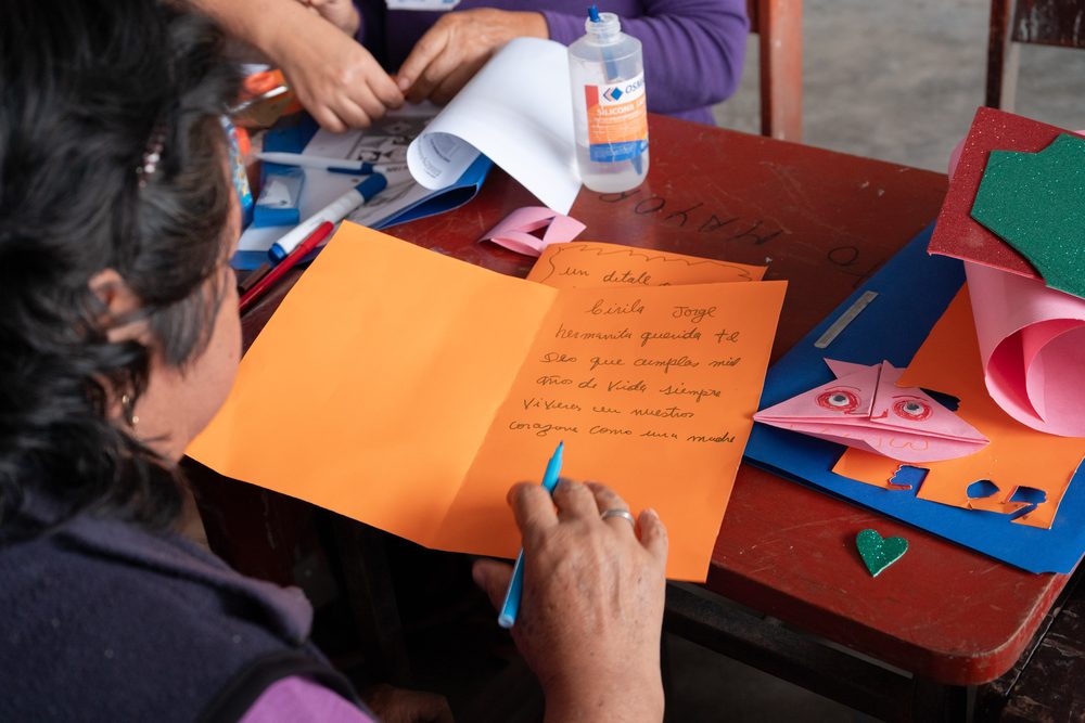 Detalle de manos escribiendo dedicatoria con plumón sobre cartel anaranjado del taller