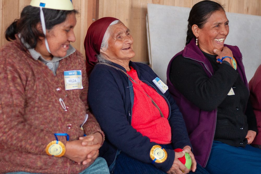 Tres adultas mayores con gorros de fiesta riendo juntas durante la celebración comunitaria